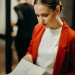 Focused woman in red blazer examining documents, symbolizing business concentration and professionalism.