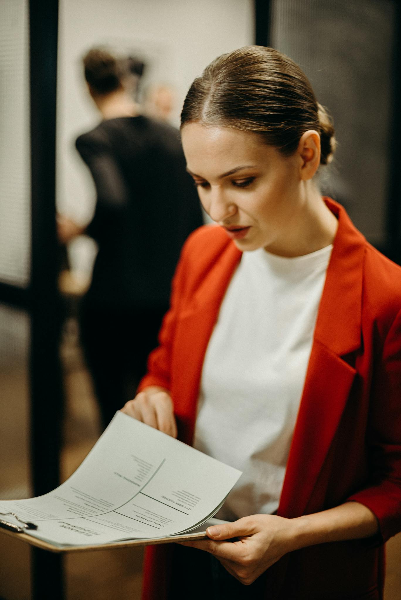 Focused woman in red blazer examining documents, symbolizing business concentration and professionalism.